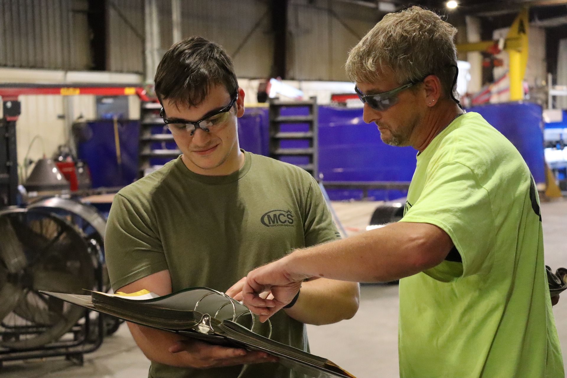 Two MCS team members reviewing bridge deck shop drawings in a binder on the shop floor