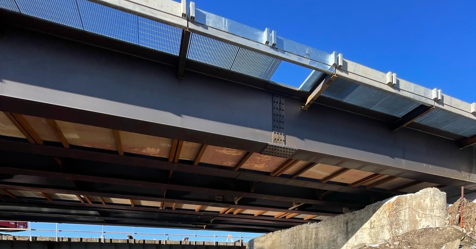 Upward view of a bridge's structural steel framing and grid decking from below